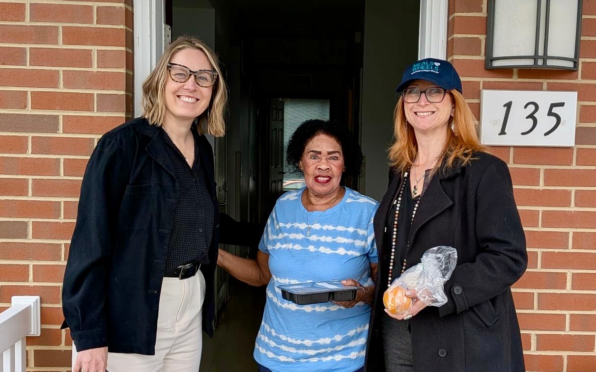 Three women standing in front of a house, smiling.